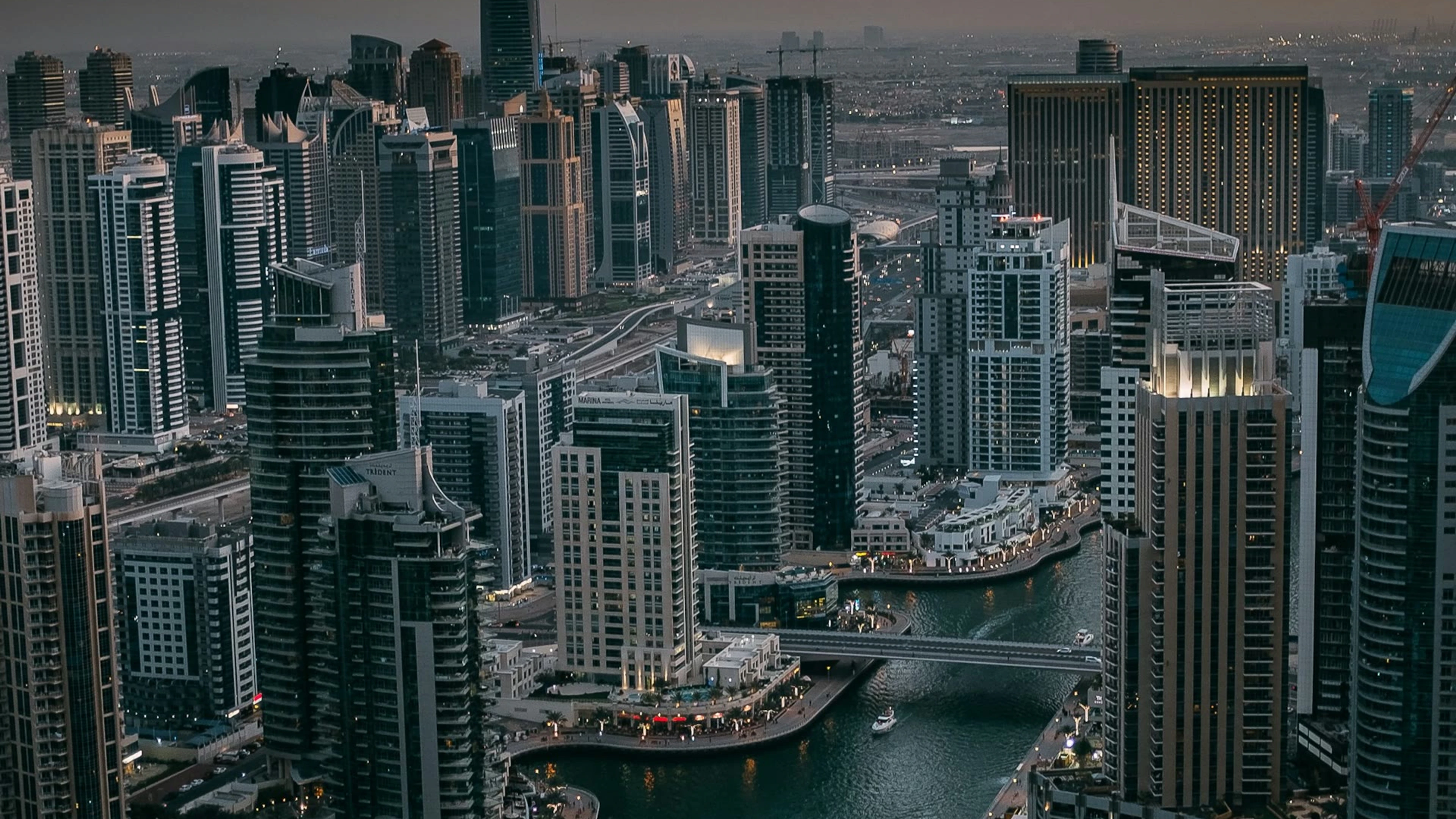 High-angle view of Dubai Marina towers, waterways and bridges at dusk.