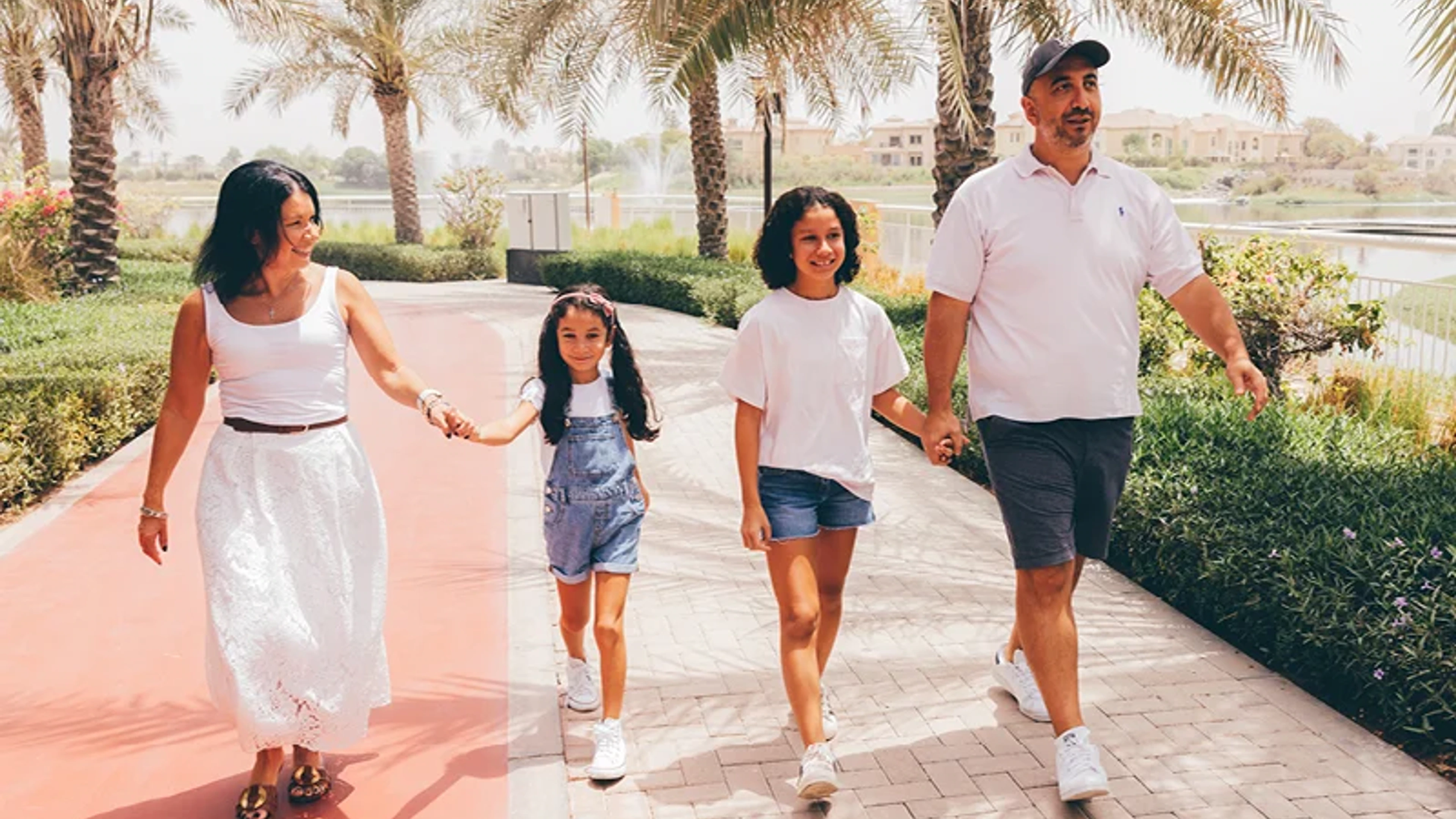 Family walking beside palms and a lagoon in a Nakheel residential community.