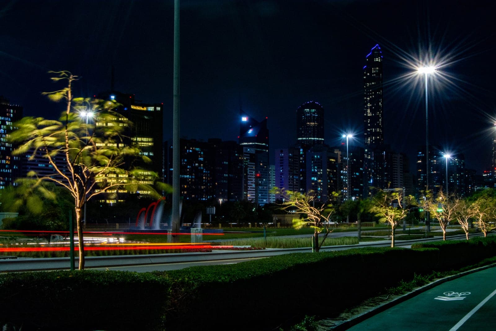Abu Dhabi's Corniche skyline at night, tower lights reflected above a tree-lined boulevard