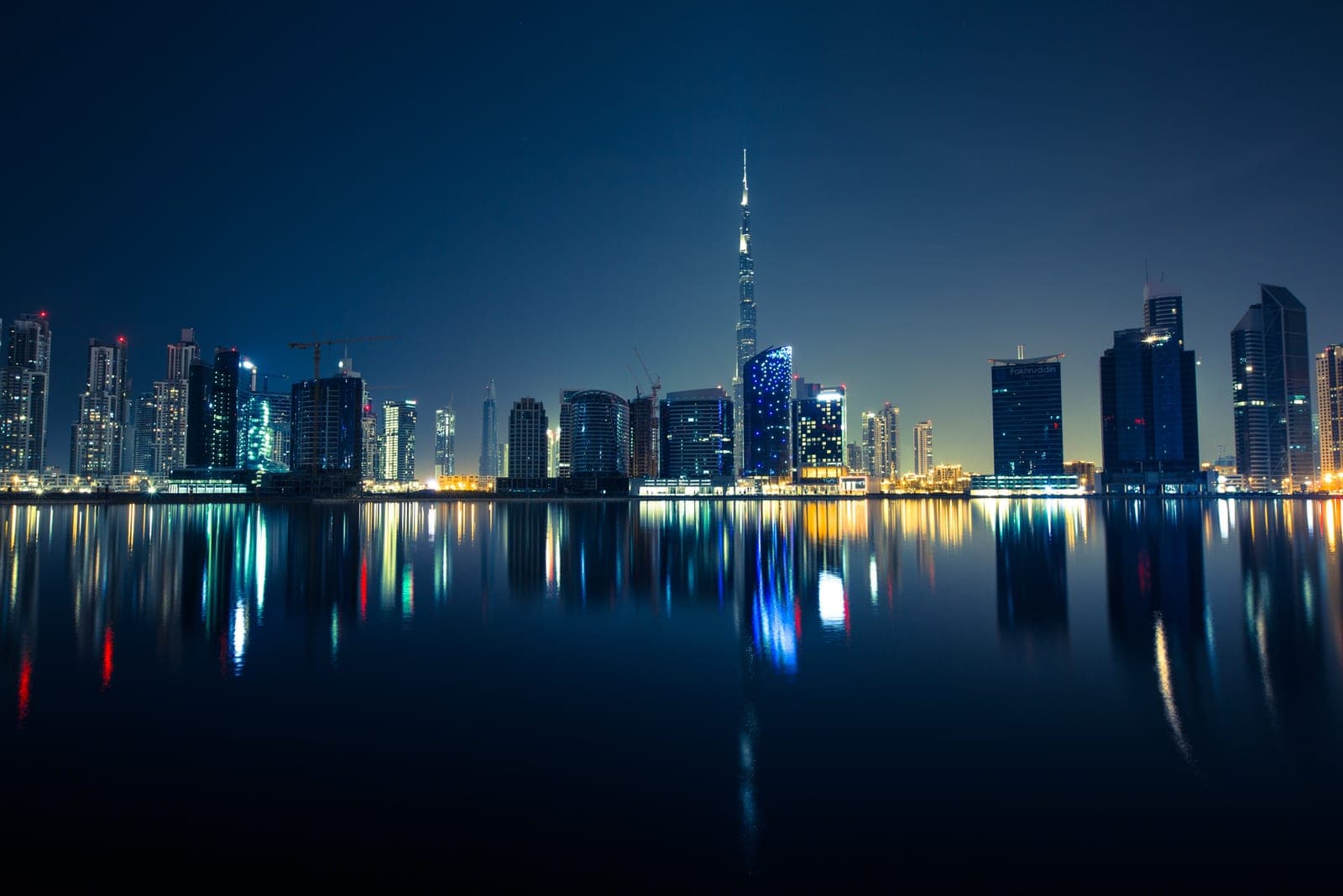 Business Bay towers and the Burj Khalifa mirrored in still water at night